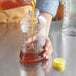 A person pouring honey into a ribbed plastic container.