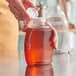 A person using a white Queenline PET honey bottle with a white plastic flip top lid to pour honey into a jar.