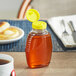 A Queenline PET honey bottle with a yellow flip top lid on a table.