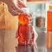 A hand holding a 16 oz. Bear PET honey bottle with a white plastic flip top lid.