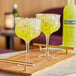 A wooden tray holding two glasses of yellow Pallini Limoncello with ice and lemons.