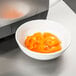 A stainless steel bowl of sliced orange bell peppers on a table.