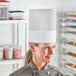 A woman wearing a Choice white disposable chef hat in a professional kitchen.