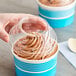 A hand holding a Choice clear plastic lid over a cup of ice cream.