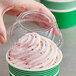 A hand holding a clear plastic cup of ice cream with a pink frosted lid and a hole in the top.