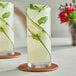 Two Acopa Collins glasses of cucumber drink with mint leaves on a white background.