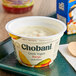 A white container of Chobani Low-Fat Mango Greek Yogurt on a table with a spoon on top.