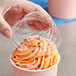 A hand holding a Choice clear plastic lid over a cup of frozen yogurt with sprinkles.