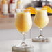 Two glasses of orange smoothie on a white counter.