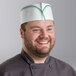 A smiling chef wearing a green striped Choice adjustable disposable overseas cap on a counter in a professional kitchen.