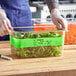 A person wearing gloves writes on a plastic container of lettuce using a Choice Green Write-On Food Pan Band.