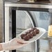 A gloved hand placing a plate of Abe's vegan chocolate brownies into a pastry case.