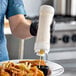 A person using a San Jamar sauce bottle to pour sauce onto a plate of fries.