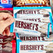 A hand holding a package of Hershey's Cookies 'n' Creme Chocolate Bars.