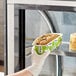 A gloved hand placing a container of Abe's vegan blueberry pound cake into a pastry case.