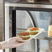 A gloved hand placing a plate of chocolate muffins into a pastry case.
