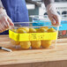 A person in blue gloves labeling a plastic container of lemons with a yellow Choice Write-On Food Pan Band.