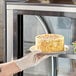 A gloved hand placing a plate of Abe's vegan vanilla-frosted layer cake into a pastry case.