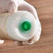 A hand in a white glove holding a San Jamar plastic squeeze bottle with a green cap.