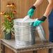 A woman in a green shirt and gloves using a Behrens galvanized steel storage can to pour sand.