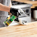 A person wearing black gloves spraying a wood surface with Seventh Generation Yuzu Basil all-purpose cleaner.