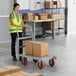 A woman in a yellow reflective vest pushing a Lavex Pro heavy-duty steel platform truck with boxes.