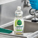 A person wearing blue gloves using Seventh Generation dish soap to clean a stainless steel sink.