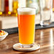 A glass of orange liquid on a table with a coaster.