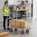 A woman in a reflective vest pushing a Lavex Pro steel platform truck with cardboard boxes on it.