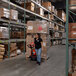 A woman in a warehouse pushing a Ballymore Lithium Battery-Powered Pallet Truck with Ballymore forks.