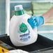 A person in blue gloves holding a bottle of Seventh Generation Free & Clear Liquid Laundry Detergent.
