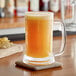 A bag of Endless Harvest Mango Aseptic Fruit Puree on a table with a glass of orange liquid on a coaster.