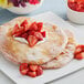 A large fry bread topped with strawberries and whipped cream on a white plate.