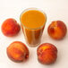 A glass of orange juice with a peach slice on the rim next to a peach.