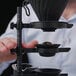 A hand placing a black Nucleus Coffee Tools chilling rock in a cup of coffee.