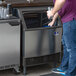 A man standing next to a Manitowoc undercounter ice machine holding a glass of ice.