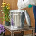 A woman pouring sand into a Behrens galvanized steel bucket with a lid.