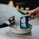 A hand using a Behrens tin funnel to pour oil into a metal container.