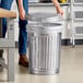 A person putting a Behrens galvanized steel trash can lid on a trash can.