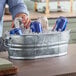 A person holding a blue can of beer in a Behrens steel tub filled with ice.