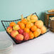 A Tablecraft Grand Master Transformer rectangular black metal basket holding a bowl of fruit on a table.