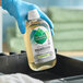 A hand in blue gloves holding a bottle of Seventh Generation Ultra-Concentrated Laundry Detergent.