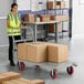 A woman in a yellow vest pushing a Lavex Pro platform truck with a group of cardboard boxes.