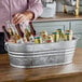 A man holding a Behrens hot-dipped steel oval tub filled with beer cans and bottles.