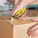 A person using a yellow and black Stanley retractable utility knife to open a box.