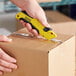 A hand using a yellow and black Stanley FATMAX utility knife to cut a box.