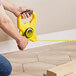 A man using a Stanley yellow fiberglass long tape measure to measure a room.