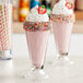 A pink milkshake with sprinkles and a straw on top.