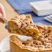 A hand cutting a piece of a chocolate chip cookie cake on a white plate.