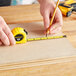 A person using a Stanley yellow measuring tape to measure a piece of wood.